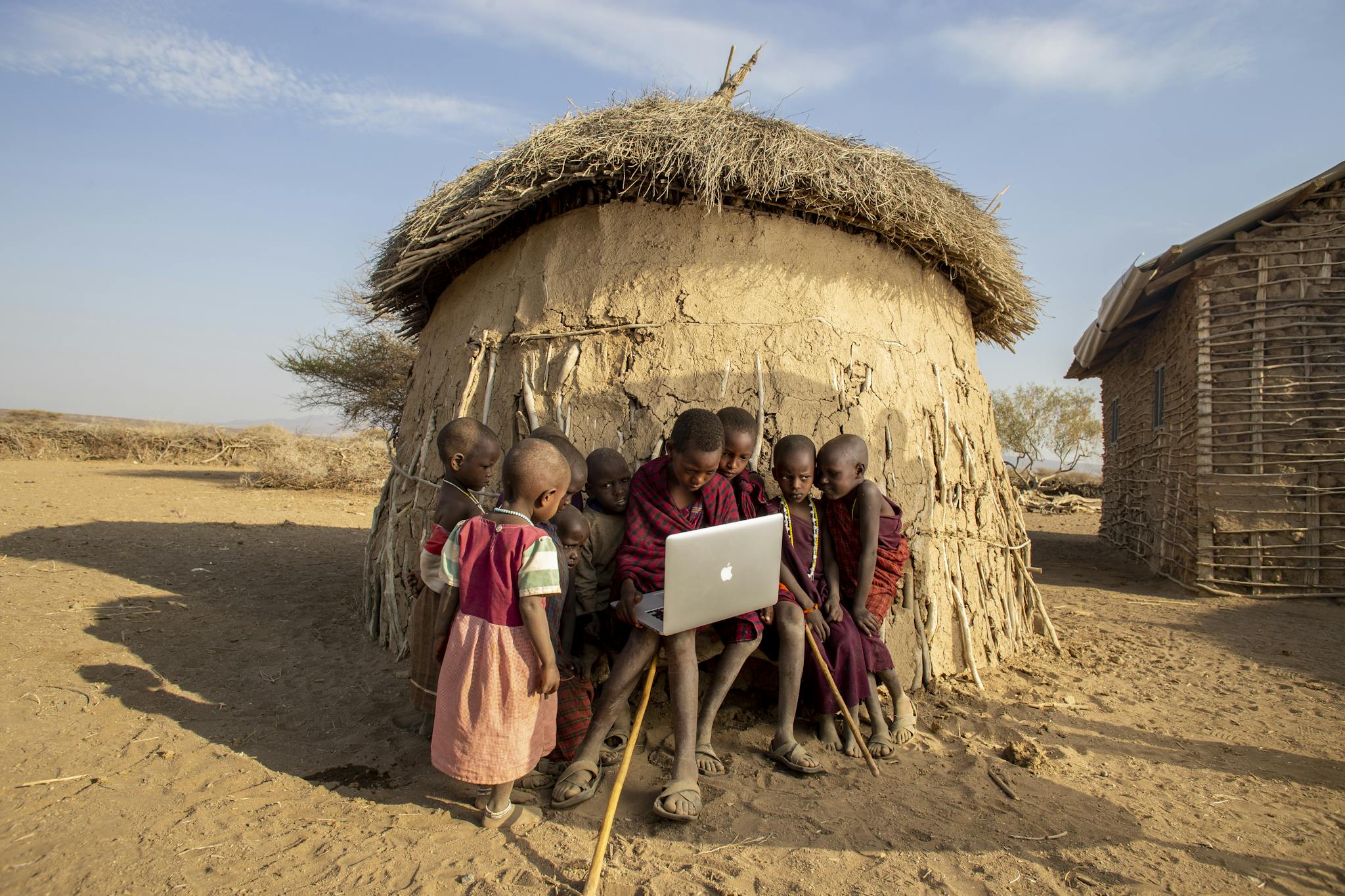 Group of African children in a Tanzanian village using a laptop outdoors, engaged in learning.